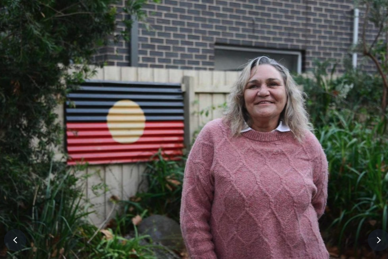 Aboriginal woman standing in front of Aboriginal flag